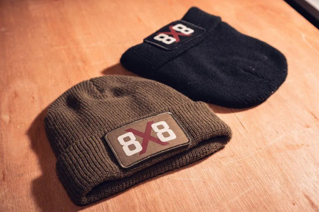 Black and military green 8x8 beanies together on a wooden workshop bench.