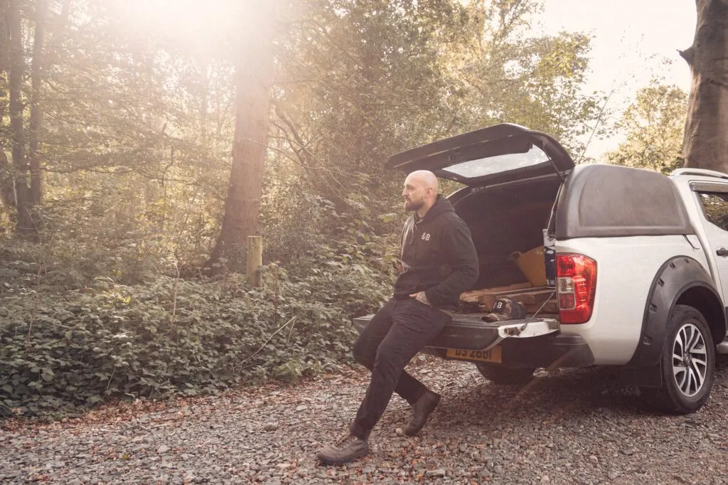 Black 8x8 hoodie worn while sitting on the tailgate of a pickup in woodland.