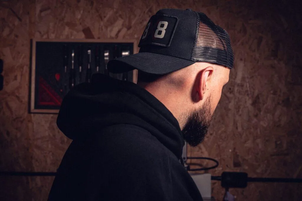 Side and rear view of the black 8x8 mesh trucker cap worn in a workshop.