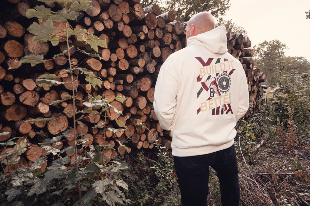Back of the Natural Raw 8x8 Build It Better hoodie showing the large graphic beside stacked timber.