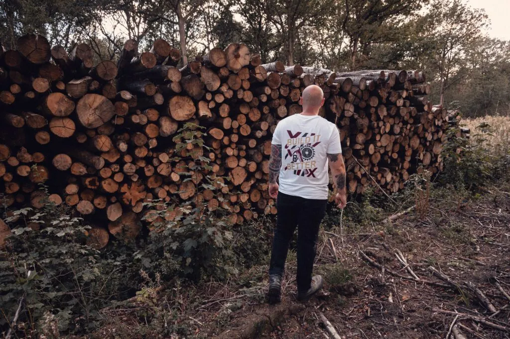 Back of the white 8x8 Build It Better T-shirt showing the graphic beside stacked timber.