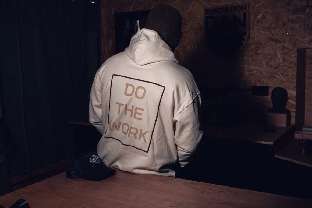 Rear view of the Raw 8x8 Do The Work hoodie in a woodworking workshop.