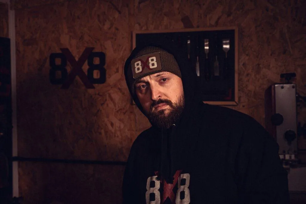 Man wearing the military green 8x8 beanie with logo patch in a workshop.