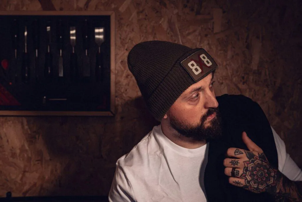 Man wearing the military green 8x8 beanie with a black hoodie over his shoulder.