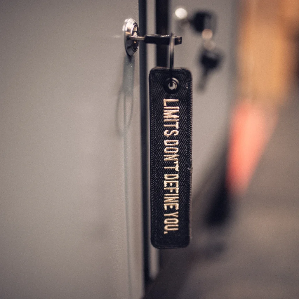 8x8 Signature Jet Tag hanging from a metal handle, showing the cream “LIMITS DON’T DEFINE YOU.” embroidery.